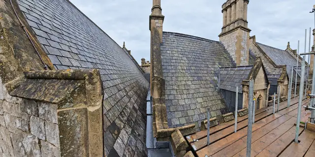 Weathered stone slate roofs and chimneys on a heritage building, viewed from scaffolding