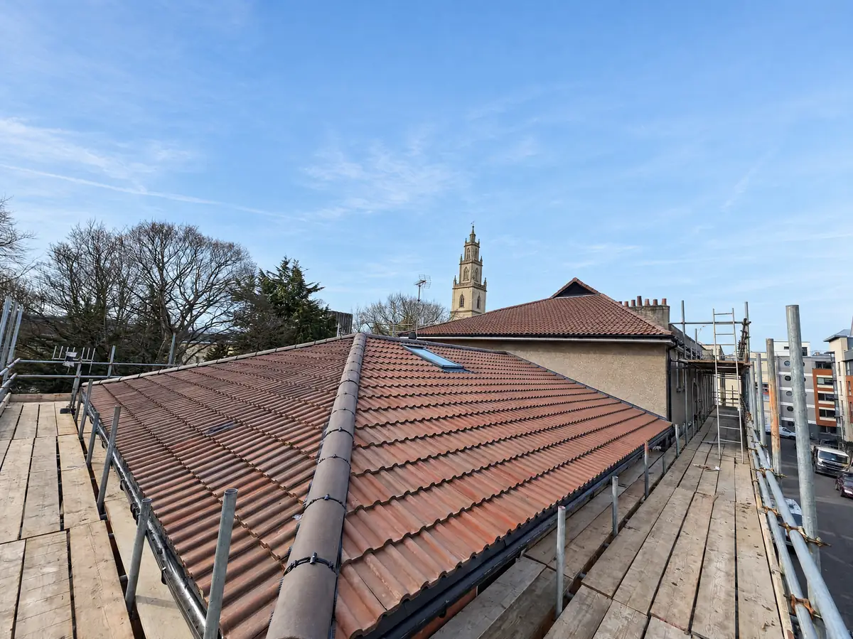 New double roman tiled hip roof with a church tower in the background