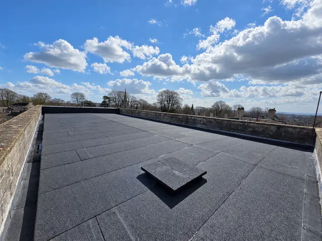 Newly laid felt flat roof with stone parapet walls under a blue sky